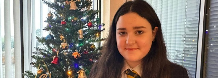 Picture of a Queen Elizabeth's winning student stood in front of a Christmas tree holding a certificate.